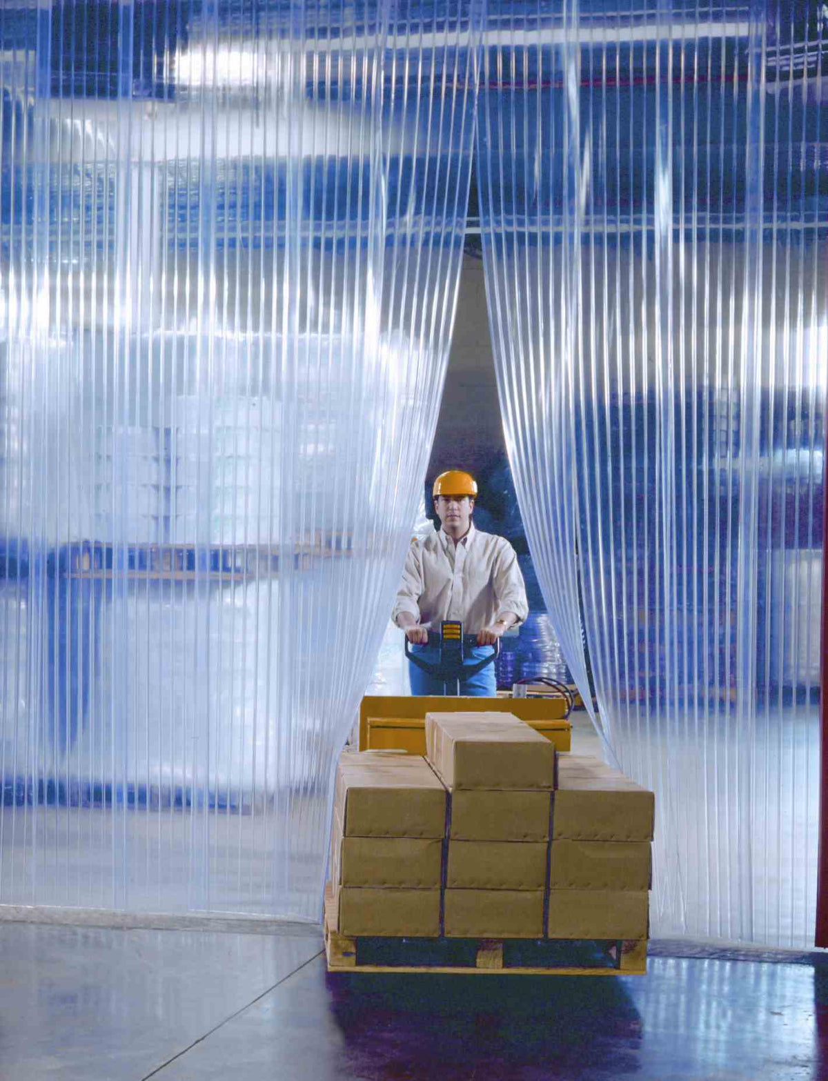 Worker moving a pallet through XPS Tech clear PVC strip curtains, 8 in × 0.080 in × 300 ft roll